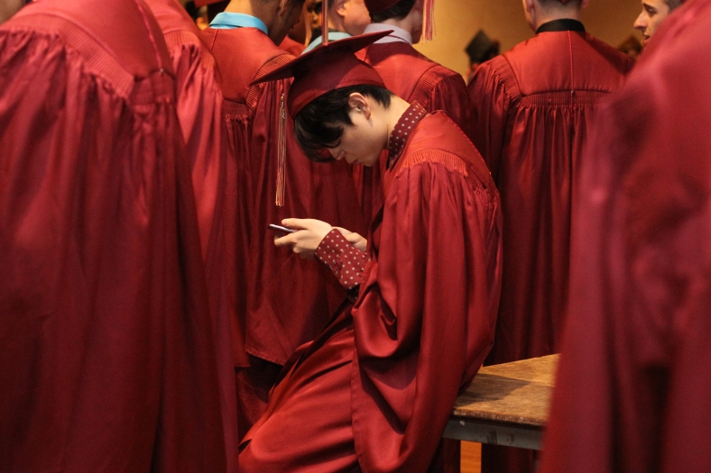 Nikos Frazier | The Vindicator A Cardinal Mooney High School student looks at his phone before lining up in Stambaugh Auditorium to receive his diploma.