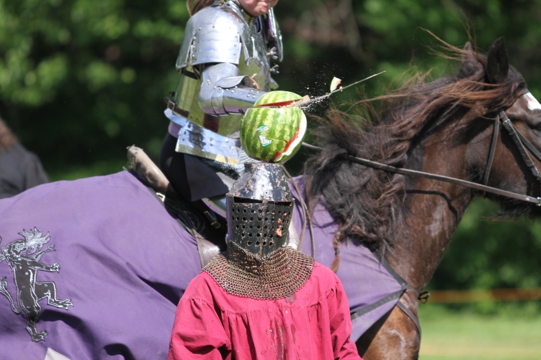 Nikos Frazier | The Vindicator Jaclyn Ziemniak(horseback) slices a watermelon atop a squire's head at the Mid-Summer Knights Medieval Festival.